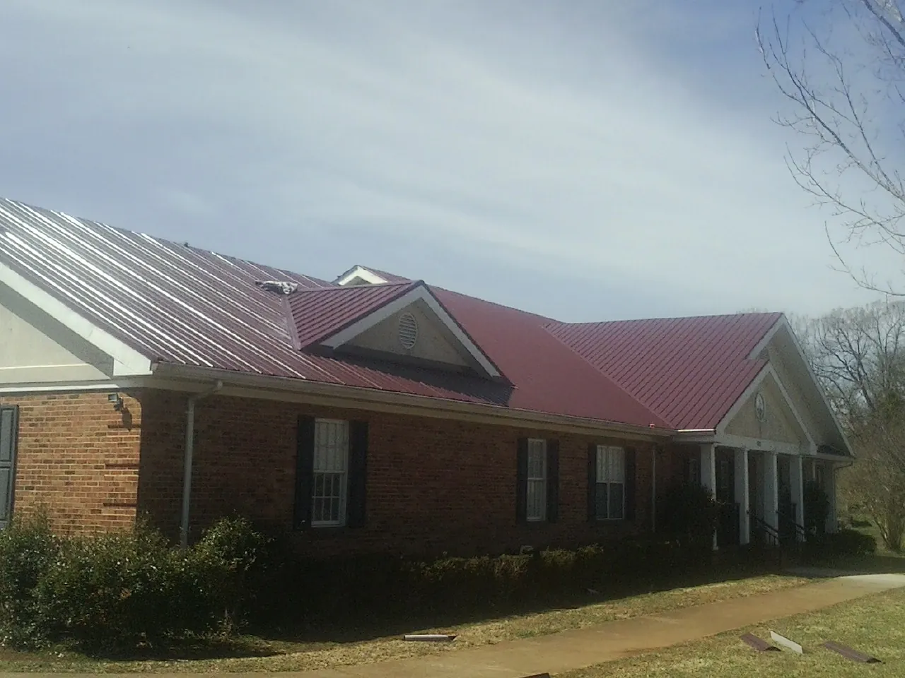 Red metal roof with gabled entries on a long brick building, from a Hail Damage Roof Repair job in Rockford