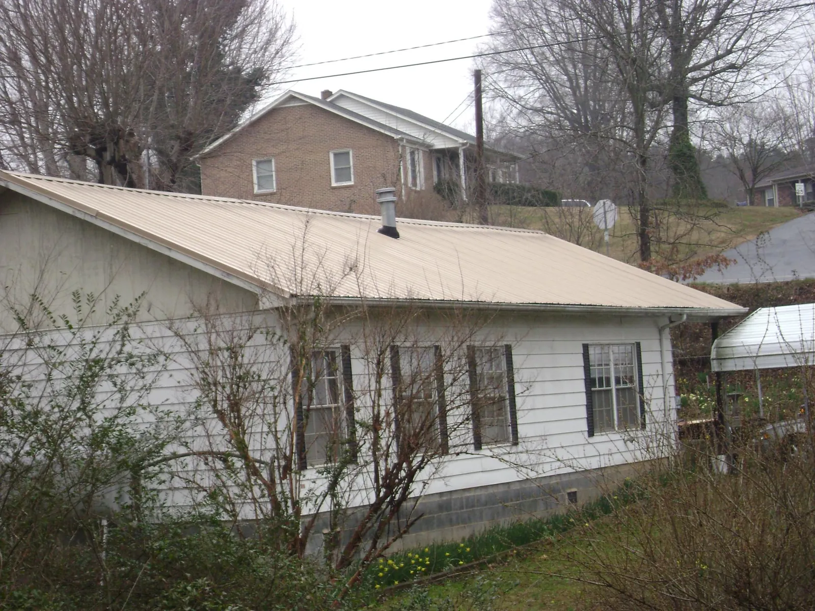 Tan metal roof on a white sided house set into a hillside — Commercial Roofing by Roofing Brothers in Rockford